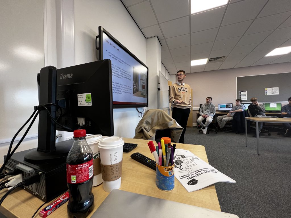 Eliot standing up talking about the slide "Who do I work with?" in the classroom.