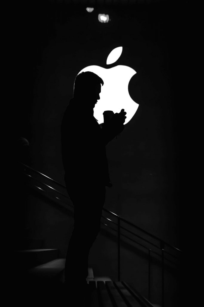 A shadow of a man standing in front of a lit up Apple logo. 