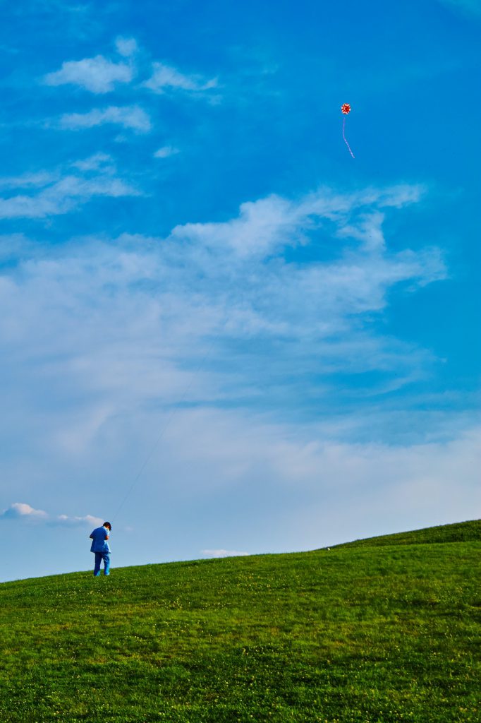 An image of a child on a green field with a blue sky above him. 