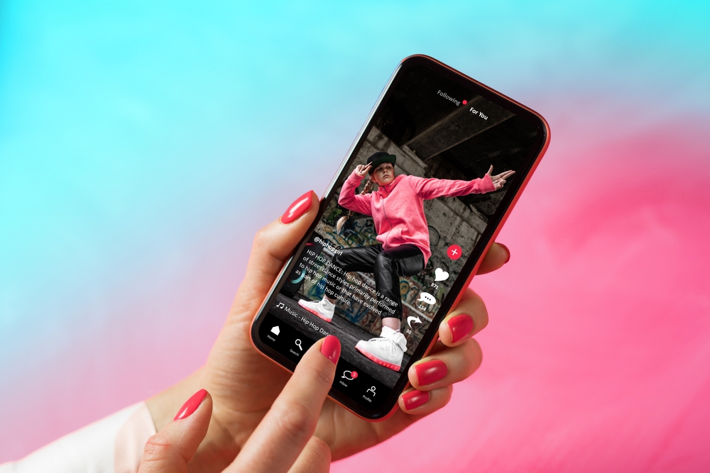 An image of a TikTok star posing on a video, displayed on an iphone with someone pointing at it. 