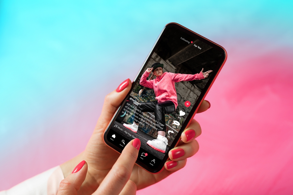An image of a TikTok star posing on a video, displayed on an iphone with someone pointing at it.