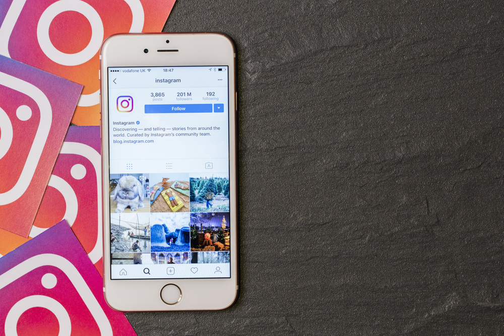 An image of a phone displaying Instagram's Instagram page. There are also instagram logos in squares behind the phone.